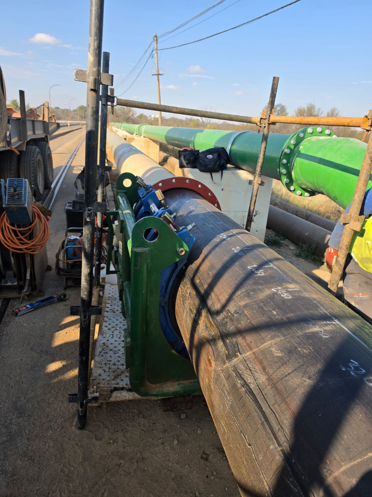 HDPE slurry pipe in a fusion machine alongside a coated steel pipeline on a bridge crossing